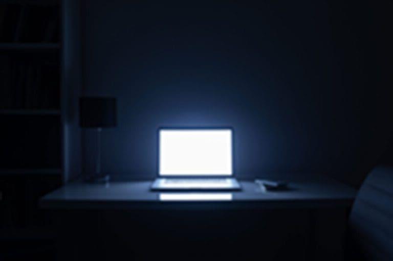 晚上房间里有电脑屏幕照明，没有人. 空荡荡的工作场所被一台笔记本电脑照亮，在黑暗中工作到很晚，加班的概念