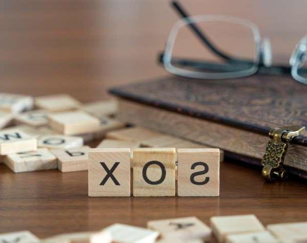 萨班斯-奥克斯利法案概念的首字母缩略词sox由木桌上的木制字母瓦片和眼镜以及一本书代表
