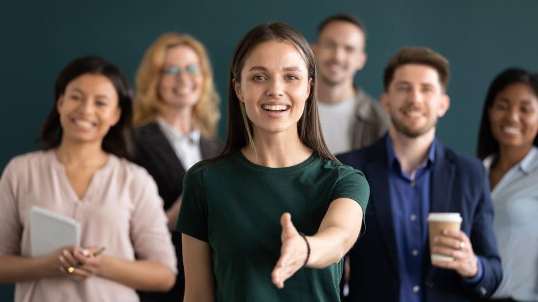 友好的年轻公司女代表伸出手与顾客握手，微笑着看着相机，与不同的同事一起摆姿势, 销售经理问候客户的概念
